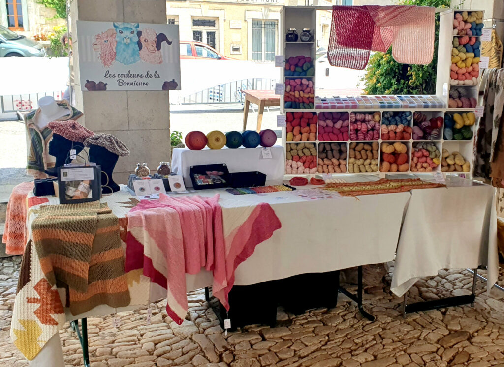 Vue générale du stand marché des Tisserands à Varaignes avec présentoir de laine et divers châles et écharpes