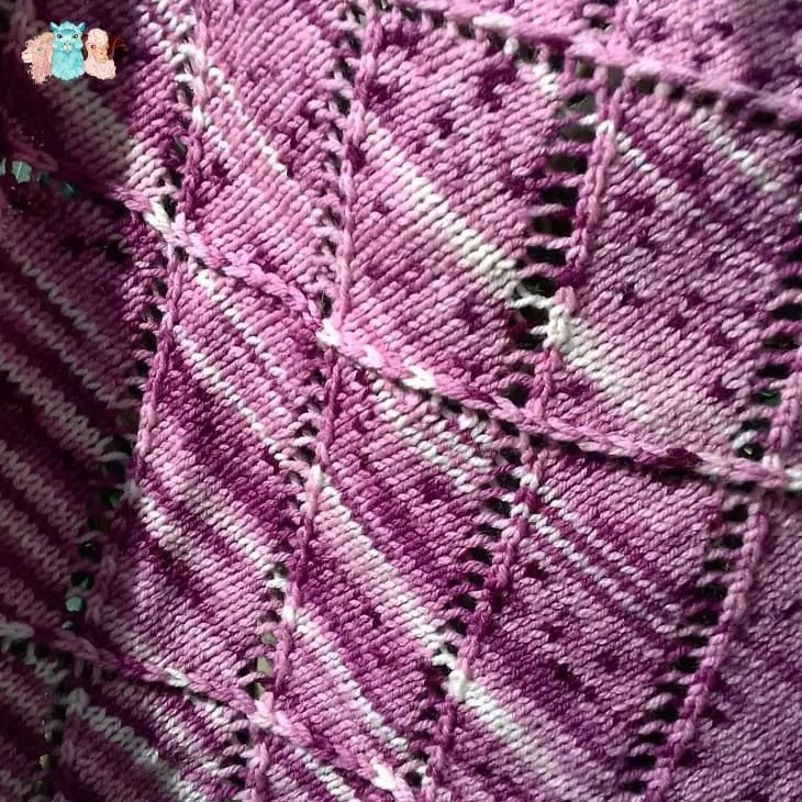 Gros plan de châle tricoté main en laine mérinos, rose-violet et écru, modèle ajouré original, accessoire fait main artisanal, idée de cadeau femme tricot unique. Fabrication française.