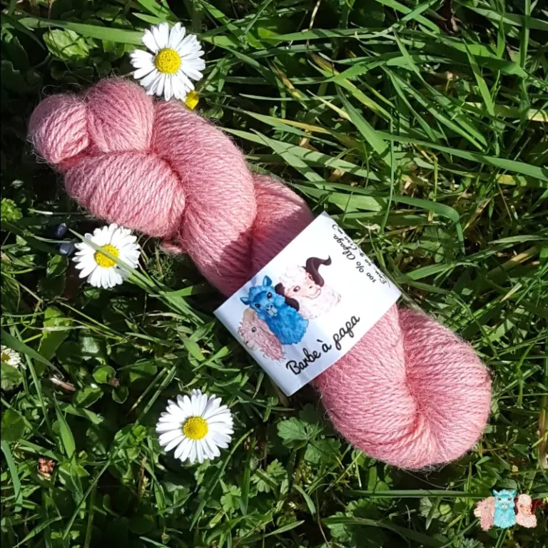 Echeveau de laine alpaga, teintée naturellement en rose tendre posée sur de l'herbe verte avec des pâquerettes. Laine artisanale, teinture végétale faite à la main en France