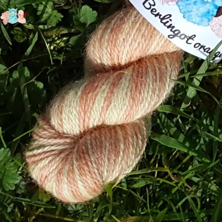 Détail écheveau de laine alpaga, teintée naturellement en nuances orangé et jaune tendre posée sur de l'herbe verte avec des pâquerettes. Laine artisanale, teinture végétale faite à la main en France