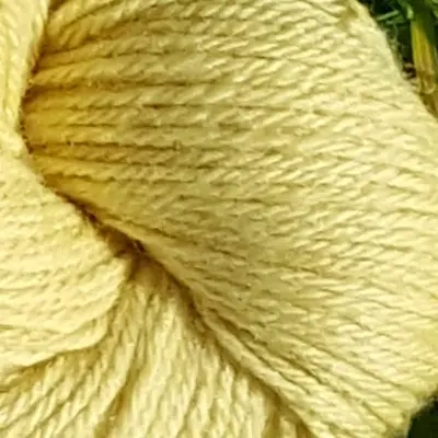 Gros plan écheveau de laine mérinos, teinté naturellement en jaune tendre posé sur de l'herbe verte avec des pâquerettes. Laine artisanale, teinture végétale faite à la main en France