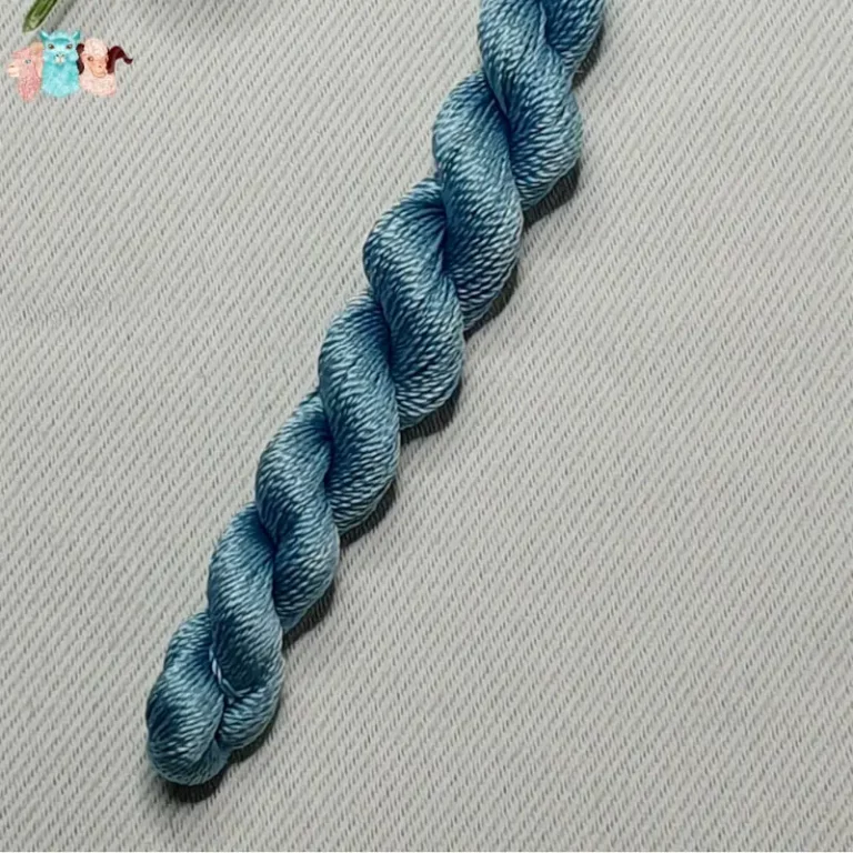 Détail d'un écheveau de fil de soie bleu avec des fleurs sur fond gris, fabriqué en france