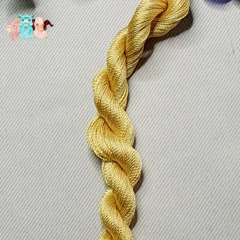 Détail d'un écheveau de fil de soie jaune clair avec des fleurs sur fond gris, fabriqué en france