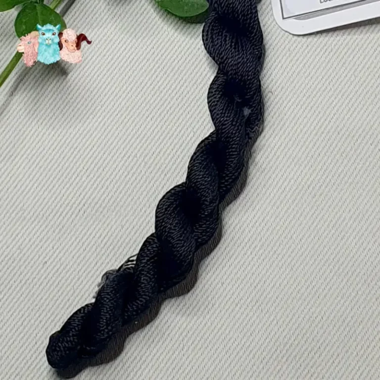 Détail d'un écheveau de fil de soie noir avec des fleurs sur fond gris, fabriqué en france