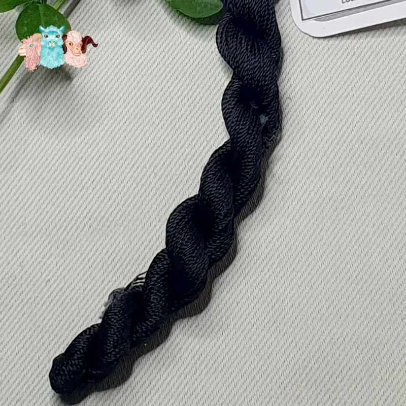 Détail d'un écheveau de fil de soie noir avec des fleurs sur fond gris, fabriqué en france