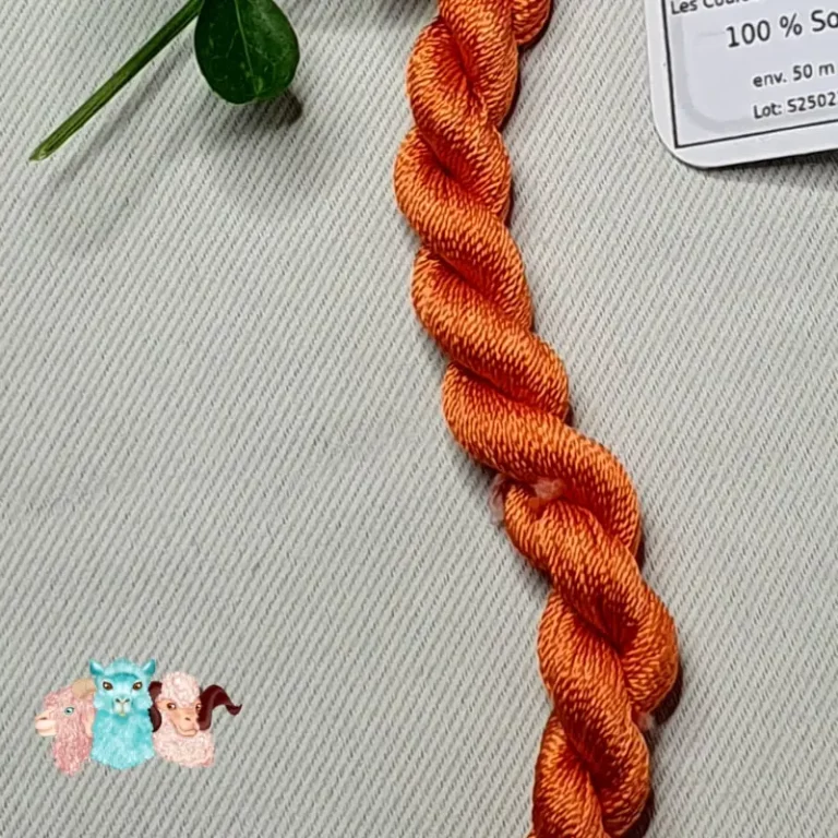 Détail d'un écheveau de fil de soie orange clair avec des fleurs sur fond gris, fabriqué en france