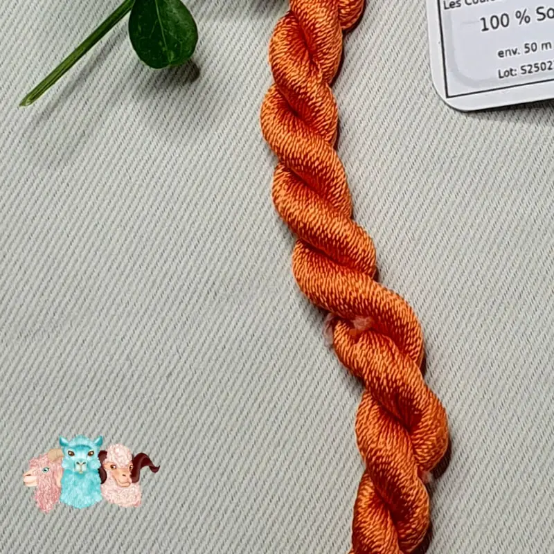 Détail d'un écheveau de fil de soie orange clair avec des fleurs sur fond gris, fabriqué en france