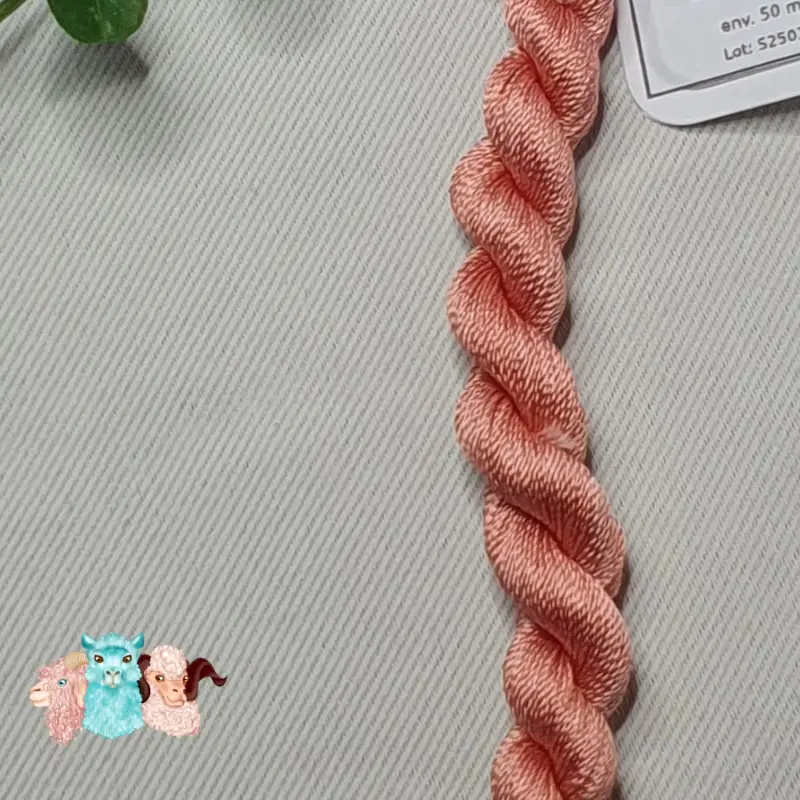 Détail d'un écheveau de fil de soie rose chair avec des fleurs sur fond gris, fabriqué en france