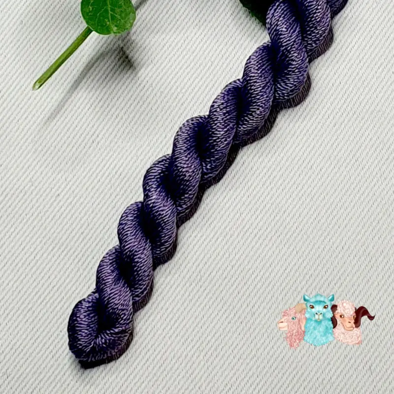 Détail d'un écheveau de fil de soie violet foncé avec des fleurs sur fond gris, fabriqué en france