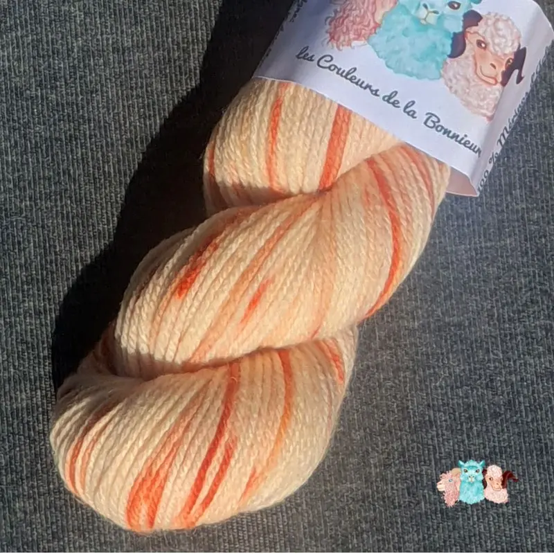 Détail d'un écheveau de laine mérinos multicolore orange et écru sur un fond gris