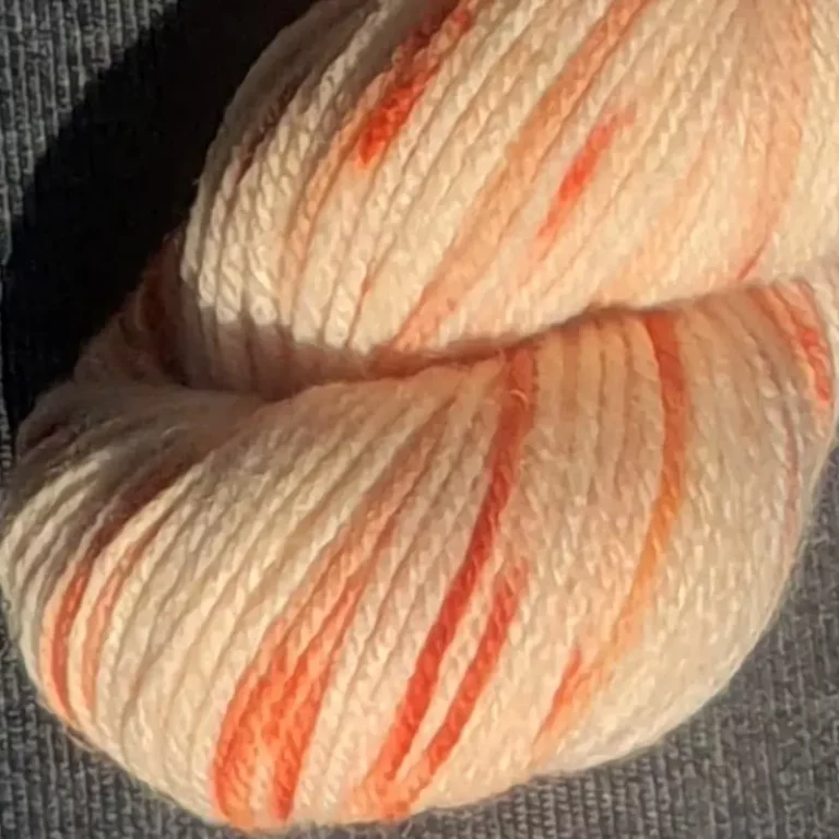 Gros plan d'un écheveau de laine mérinos multicolore orange et écru sur un fond gris