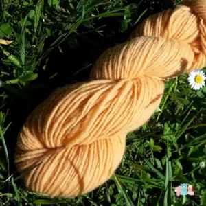 Détail d'un écheveau de laine française fil mèche fin coloris jaune doré sur fond d'herbe avec des fleurs fabriqué en france