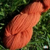 Détail d'un écheveau de laine française fil mèche fin coloris orange sur fond d'herbe avec des fleurs fabriqué en france