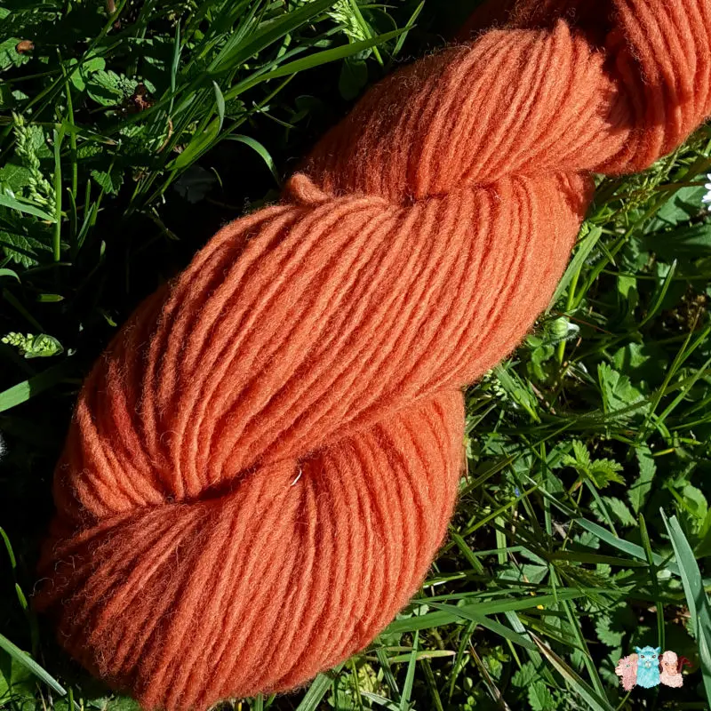 Détail d'un écheveau de laine française fil mèche fin coloris orange sur fond d'herbe avec des fleurs fabriqué en france