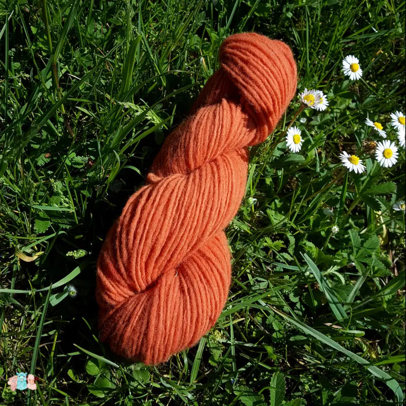 Echeveau de laine française fil mèche fin coloris orange sur fond d'herbe avec des fleurs fabriqué en france