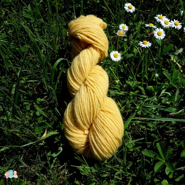 Echeveau de laine française fil mèche fin coloris jaune sur fond d'herbe avec des fleurs fabriqué en france