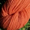 Gros plan d'un écheveau de laine française fil mèche fin coloris orange sur fond d'herbe avec des fleurs fabriqué en france