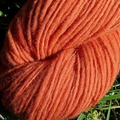 Gros plan d'un écheveau de laine française fil mèche fin coloris orange sur fond d'herbe avec des fleurs fabriqué en france