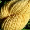 Gros plan d'un écheveau de laine française fil mèche fin coloris jaune sur fond d'herbe avec des fleurs fabriqué en france