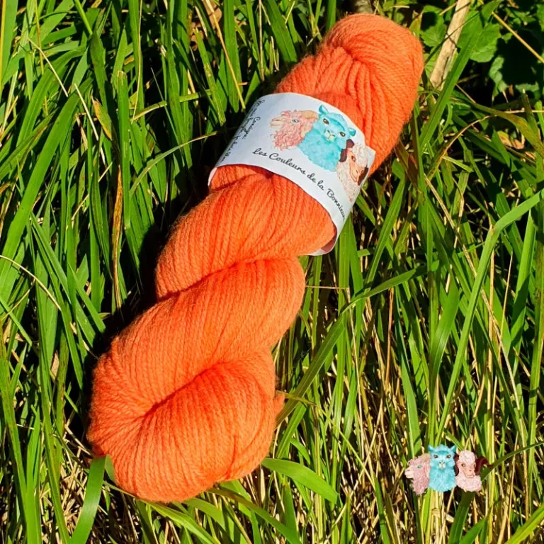 Echeveau de laine mérinos unie, teinté naturellement en orange posé sur fond d'herbe verte, teinture végétale faite à la main en France