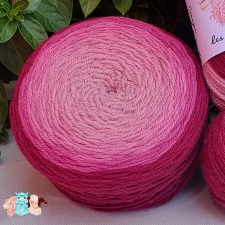 Détail d'une pelote de laine de coloris du violet foncé au violet clair devant des feuilles vertes et posé sur un fond gris.