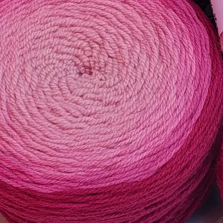 Gros plan d'une pelote de laine de coloris du violet foncé au violet clair devant des feuilles vertes et posé sur un fond gris.