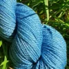Gros plan d'un écheveau de laine mérinos soie teinté en bleu sur un fond d'herbe verte.
