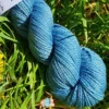 Détail d'un écheveau de laine mérinos soie teinté en bleu sur un fond d'herbe verte.