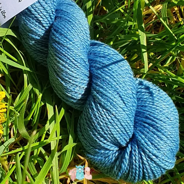 Détail d'un écheveau de laine mérinos soie teinté en bleu sur un fond d'herbe verte.