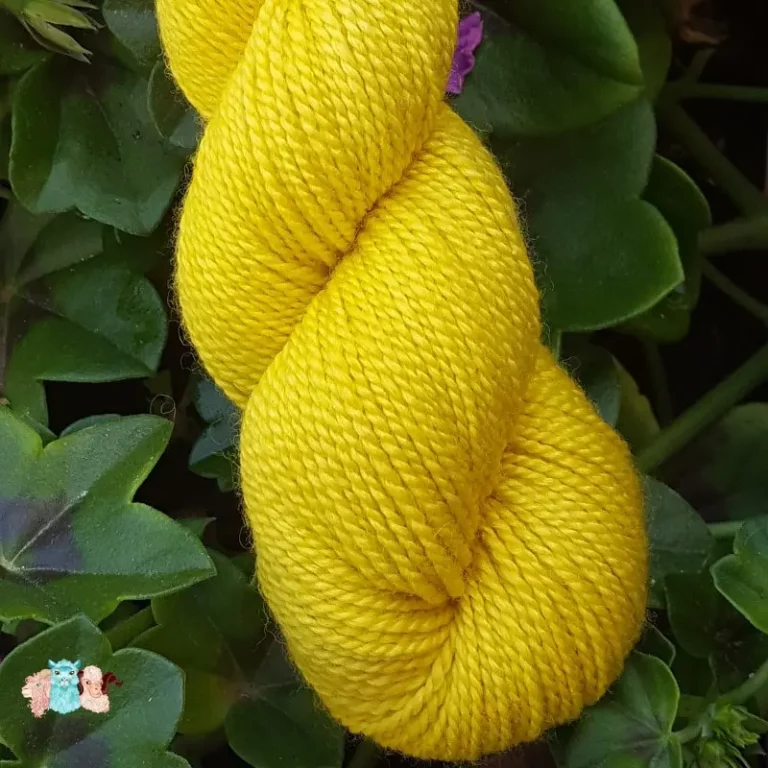 Détail d'un écheveau de laine mérinos soie teinté en jaune intense sur un fond d'herbe verte.
