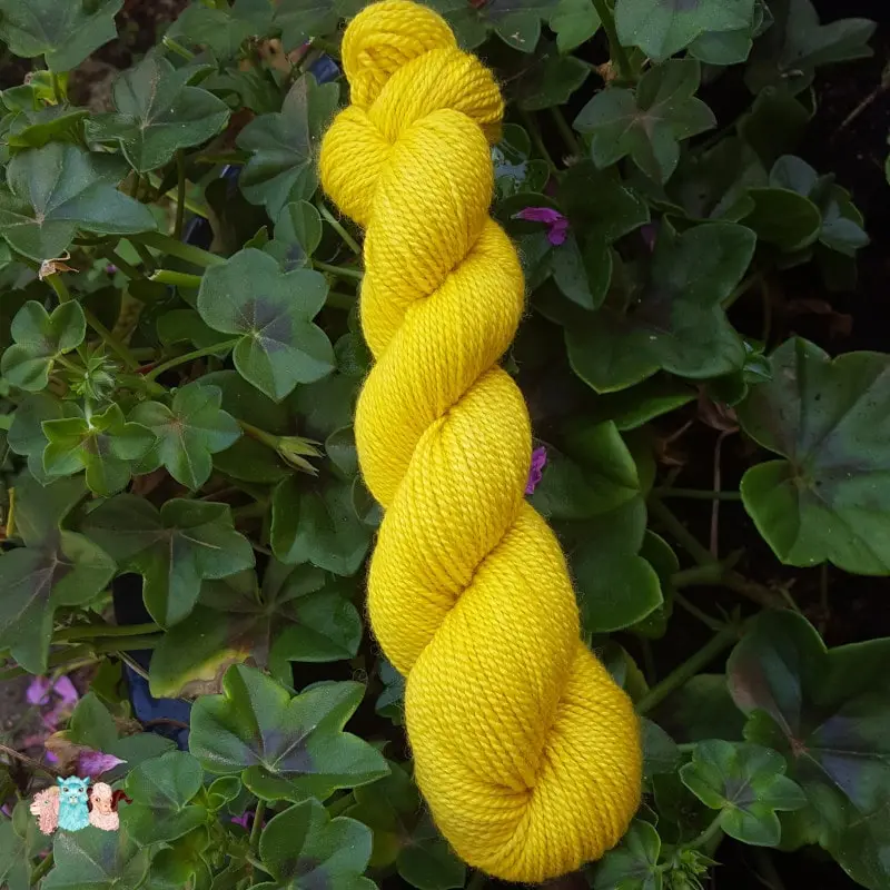 Echeveau de laine mérinos soie teinté en jaune intense sur un fond d'herbe verte.