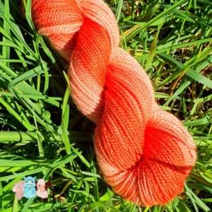 Détail d'un écheveau de laine mérinos soie teinté en orange nuancé sur un fond d'herbe verte.