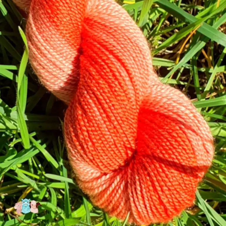 Gros plan d'un écheveau de laine mérinos soie teinté en orange nuancé sur un fond d'herbe verte.