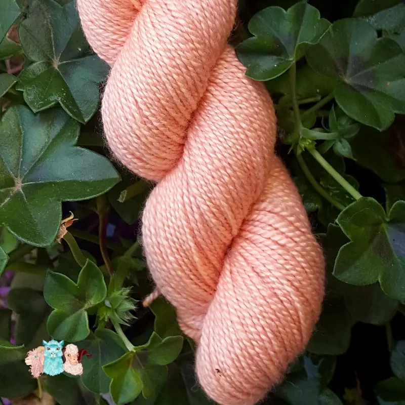 Détail d'un écheveau de laine mérinos soie teinté en orange rouge clair sur un fond d'herbe verte.