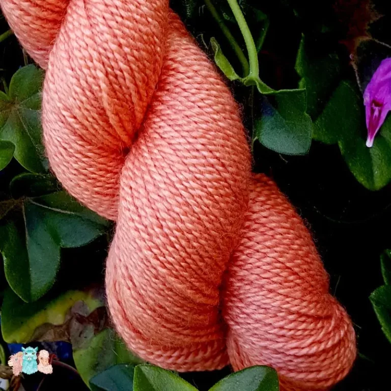 Détail d'un écheveau de laine mérinos soie teinté en orange rouge sur un fond d'herbe verte.