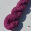 Détail d'un écheveau de laine mérinos unie, teinté naturellement en violet foncé posé sur fond gris, teinture végétale faite à la main en France