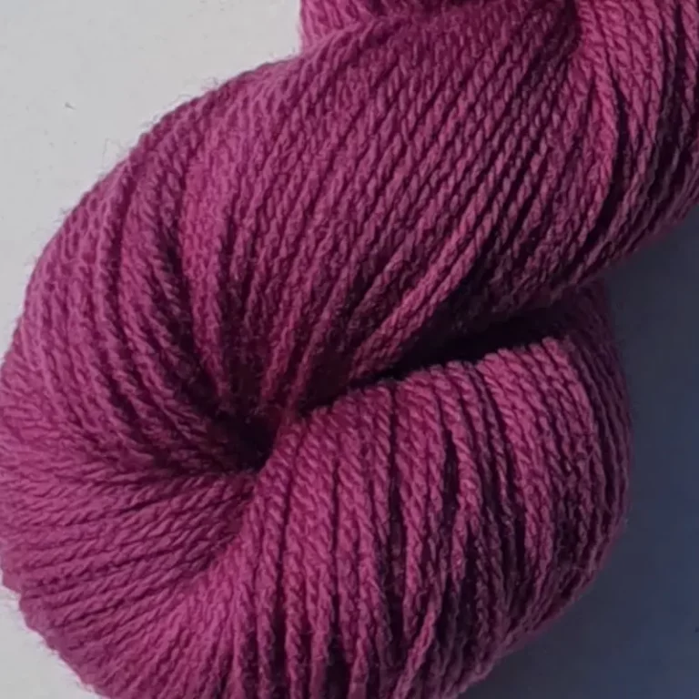 Gros plan d'un écheveau de laine mérinos unie, teinté naturellement en violet foncé posé sur fond gris, teinture végétale faite à la main en France