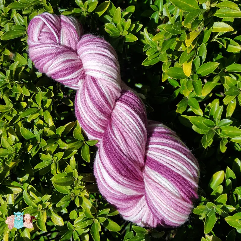 Echeveau de laine mérinos multicolore violet avec des nuances sur un fond de feuilles vertes