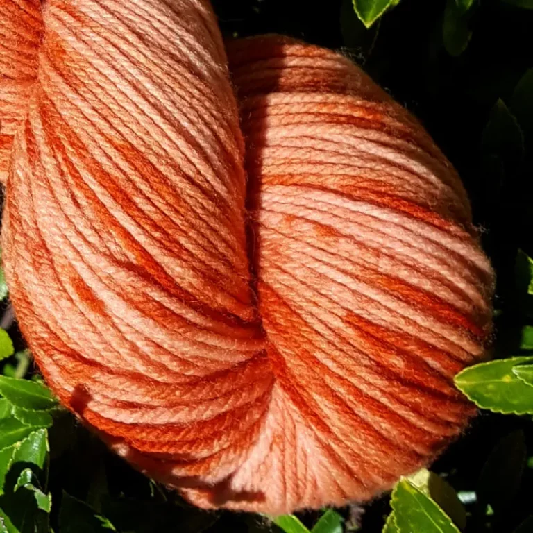 Gros plan d'un écheveau de laine mérinos multicolore orange avec des nuances sur un fond de feuilles vertes