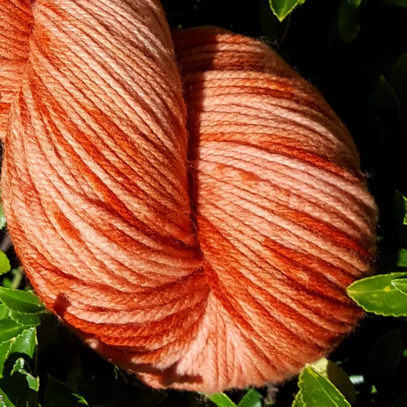 Gros plan d'un écheveau de laine mérinos multicolore orange avec des nuances sur un fond de feuilles vertes