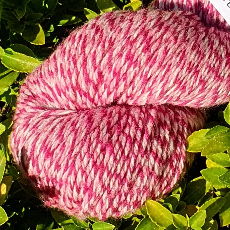 Gros plan d'un écheveau de laine chinée violette, sur fond de feuilles vert, fabrication française