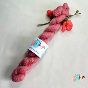 Echeveau laine dentelle rose violet, fil lace teinté naturellement avec une fleur rouge, fond gris.