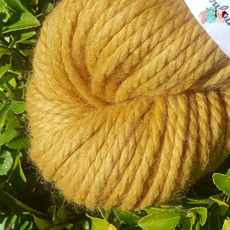 Détail d'un écheveau de laine mérinos alpaga teinté en jaune doré sur un fond de feuilles vertes.