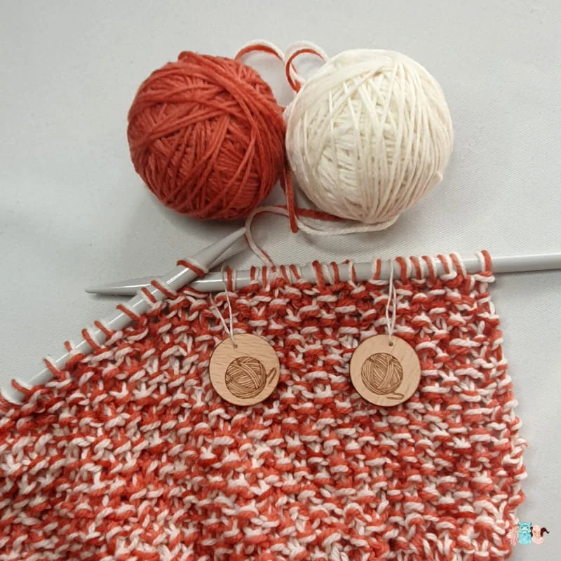 Tricot en cours avec des aiguilles avec une pelote écrue et une orangée avec des marqueurs de maille.