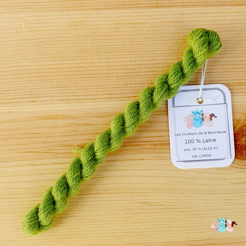 Détail d'un écheveau de fil de laine vert clair sur fond bois, fabriqué en france