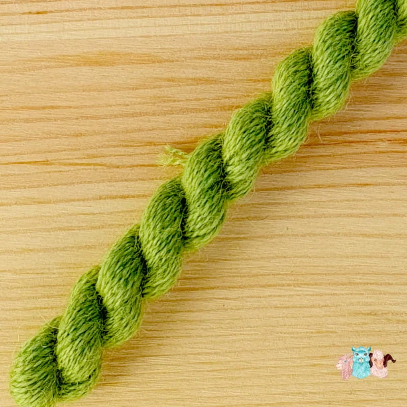 Détail d'un écheveau de fil de laine vert clair sur fond bois, fabriqué en france