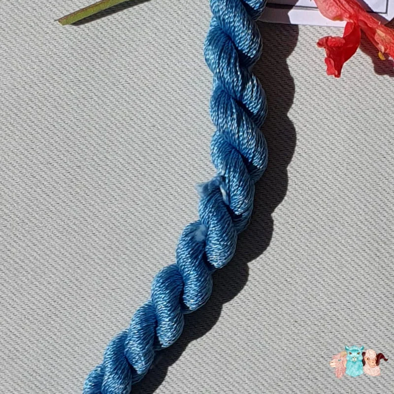 Détail d'un écheveau de fil de soie bleu indigo clair avec des fleurs sur fond gris, fabriqué en france