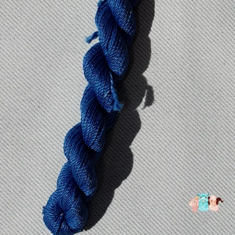 Détail d'un écheveau de fil de soie bleu indigo foncé avec des fleurs sur fond gris, fabriqué en france