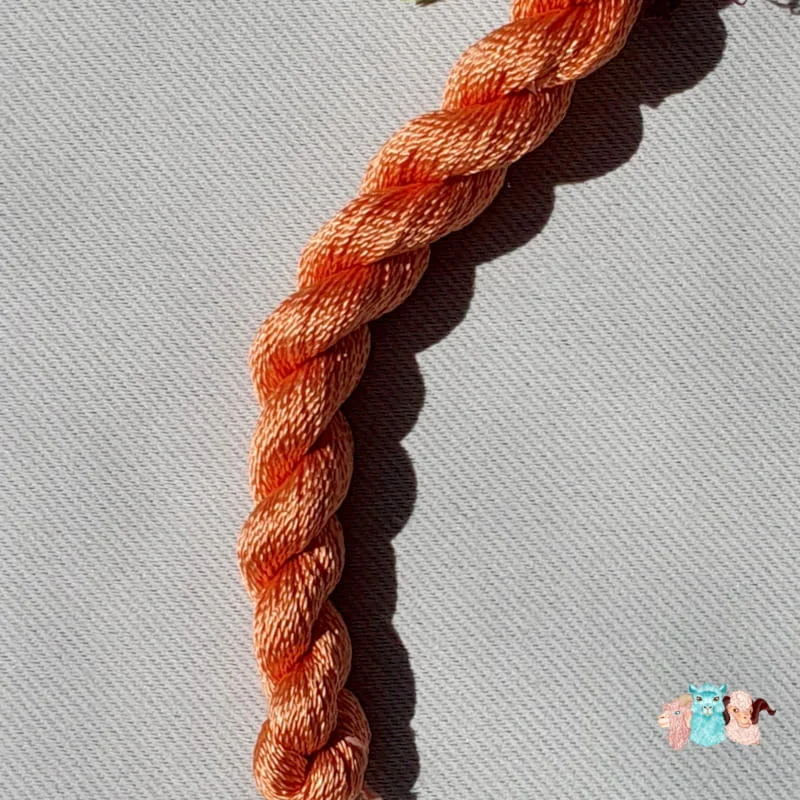 Détail d'un écheveau de fil de soie orange clair avec des fleurs sur fond gris, fabriqué en france