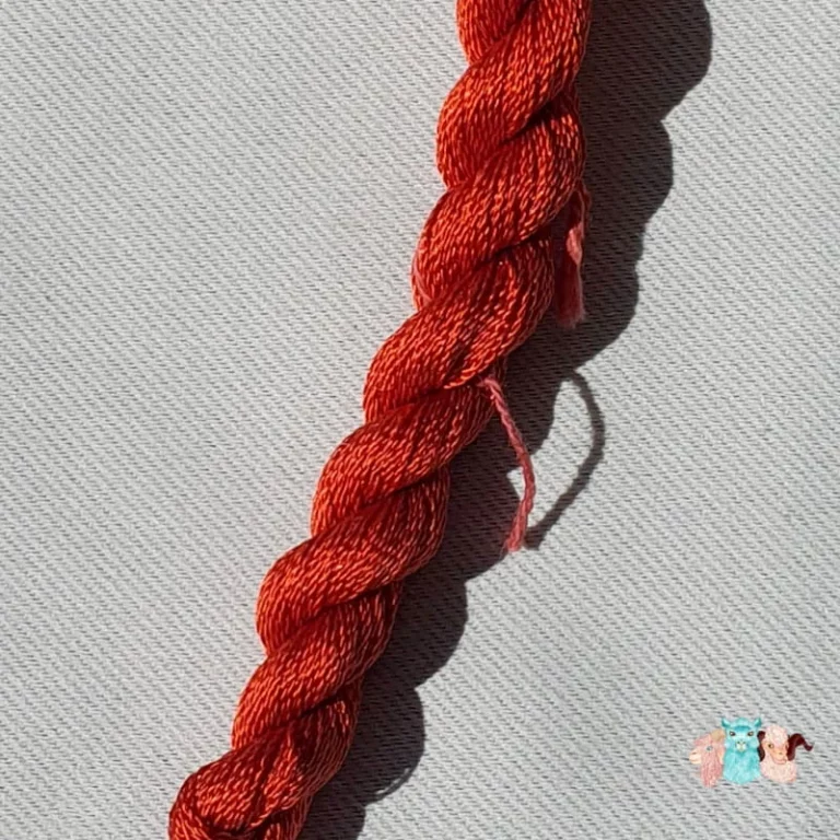 Détail d'un écheveau de fil de soie orange foncé avec des fleurs sur fond gris, fabriqué en france